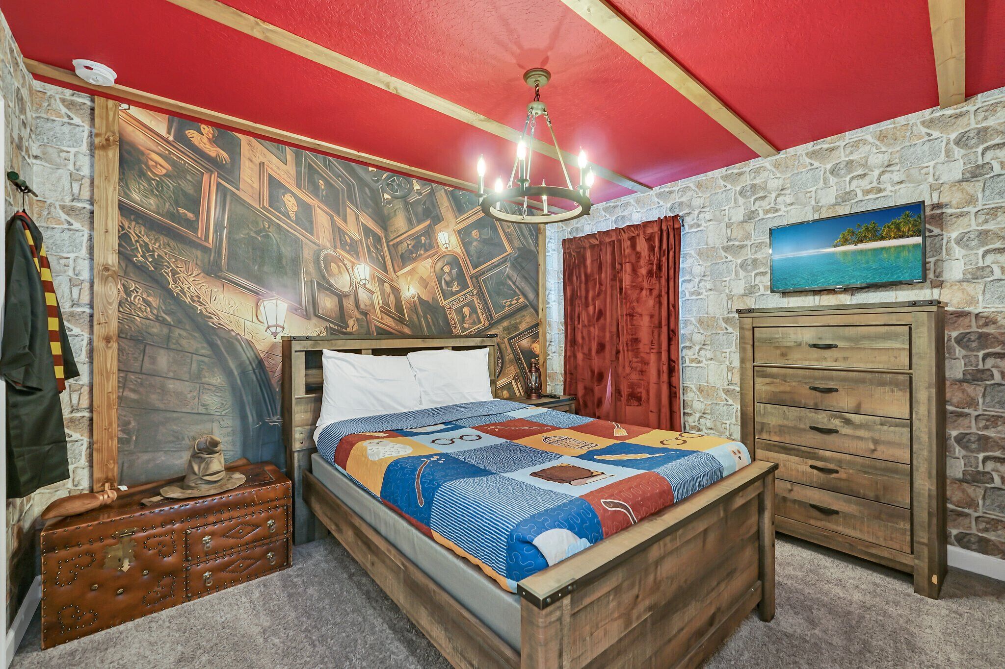 A room with a wooden bed, a stone wall, a red ceiling, a chandelier, a wooden dresser, and a painting of a beach.