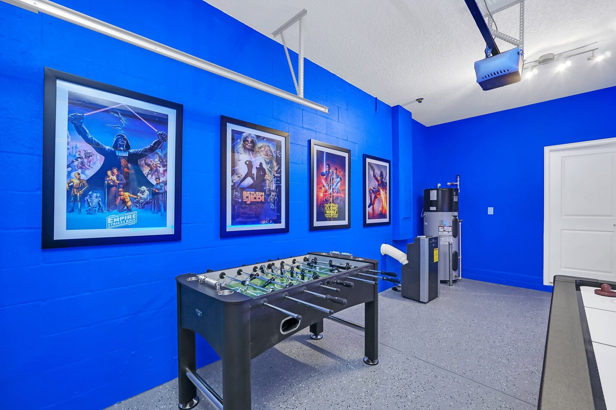 Ein Zimmer mit blauen Wänden, einem Kicker und gerahmten Filmplakaten an der Wand.