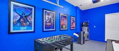 Ein Zimmer mit blauen Wänden, einem Kicker und gerahmten Filmplakaten an der Wand.
