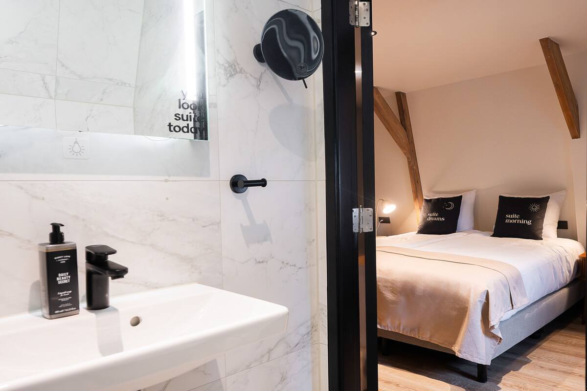Un baño moderno con lavamanos de mármol blanco, dispensador de jabón negro y ducha.