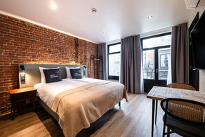 Ein Hotelzimmer mit Backsteinwand, einem großen Bett mit Kissen, einem Holztisch und Blick durch ein Fenster.