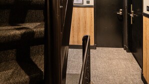 Un escalier recouvert de moquette, doté d’une rampe, avec un mur en bois et une porte en bas.