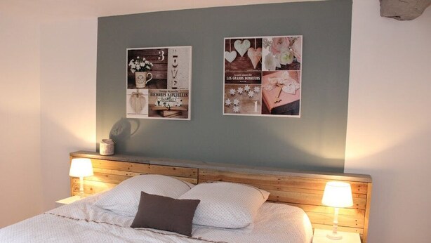 A bedroom with a wooden headboard, a bed with white bedding, two bedside lamps, and two framed pictures on the wall.