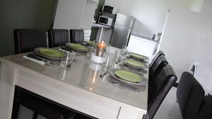 A dining table set with green plates, silverware, and a candle. There are black chairs around the table.