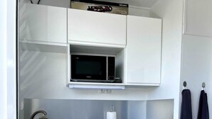 A compact kitchen with white cabinets, a microwave, a sink, and a small countertop. - Chez Valerie ET Pascal (Tartane)