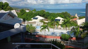 A coastal view with a pool area, palm trees, and buildings with solar panels. - Chez Valerie ET Pascal (Tartane)