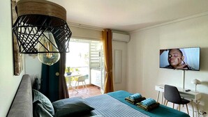 A hotel room with a bed, a desk, a television, and a balcony with a chair. - Chez Valerie ET Pascal (Tartane)