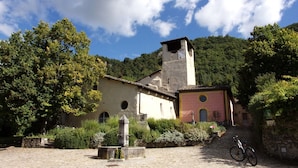 A historic building with a bell tower, surrounded by lush greenery and a cobblestone path. - Chambre d'Hôtes l'Hôsting Noix (Hostun)