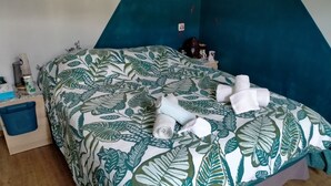 A bed with a leaf-patterned bedspread, a blue nightstand with a blue storage bin, and a teal accent wall. - Chambre d'Hôtes l'Hôsting Noix (Hostun)