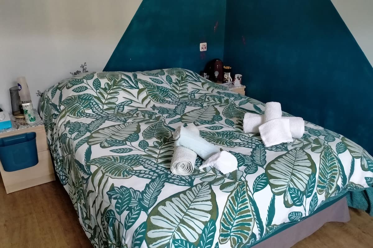 A bed with a leaf-patterned bedspread, a blue nightstand with a blue storage bin, and a teal accent wall.