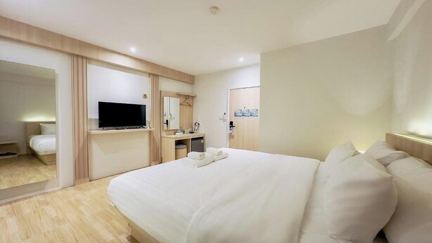 A modern hotel room with a large bed, a TV, a mirror, and a small desk with a chair. - Zhennan Teabar Hotel (Chiang Mai)