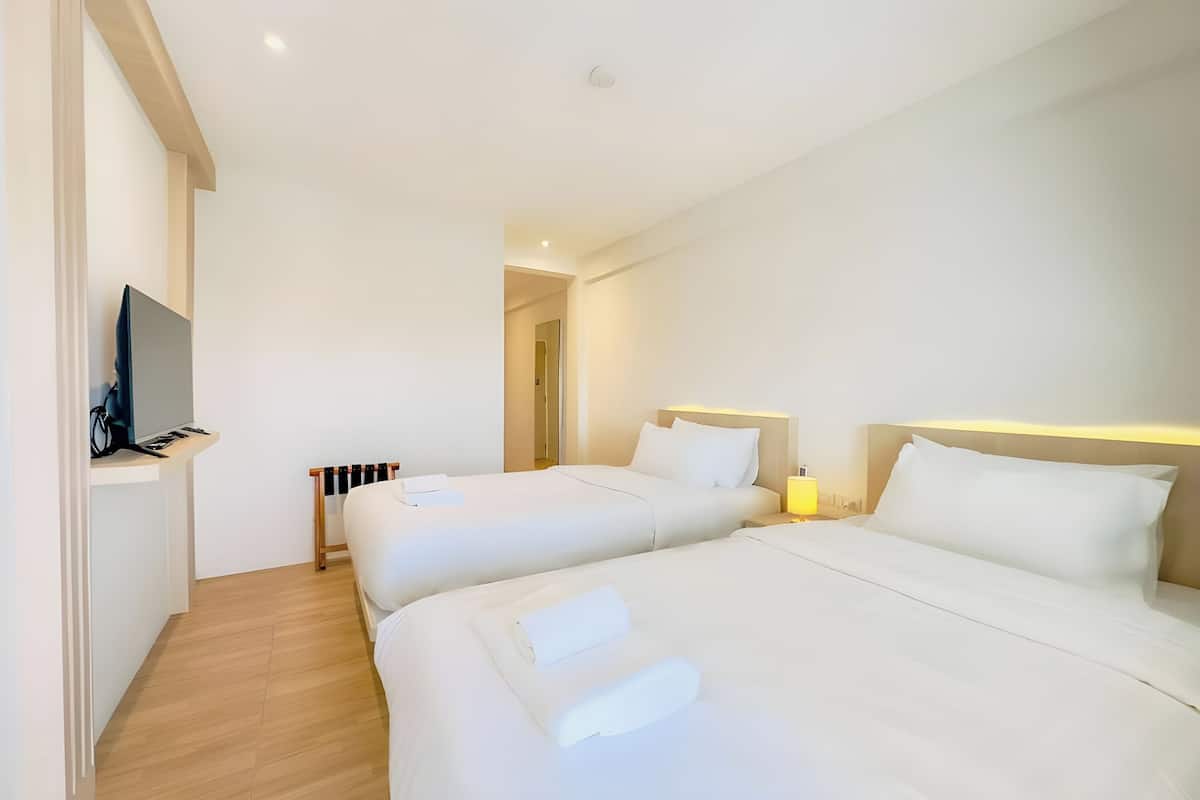 Quarto de hotel com duas camas, televisão e mesa de cabeceira.