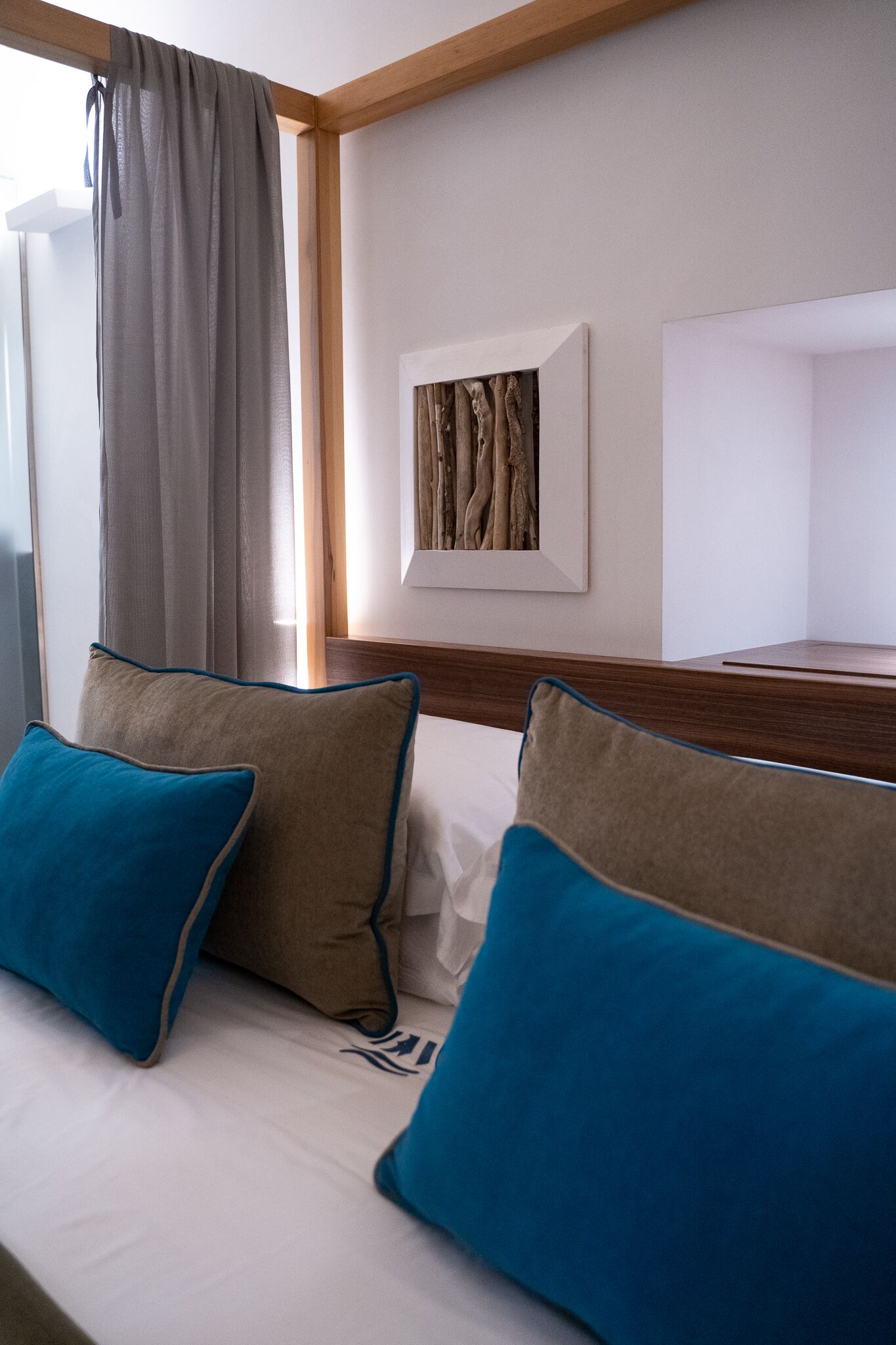 Ein Hotelzimmer mit einem Bett, zwei Kissen, einem Fenster mit Vorhängen und einem gerahmten Bild an der Wand.