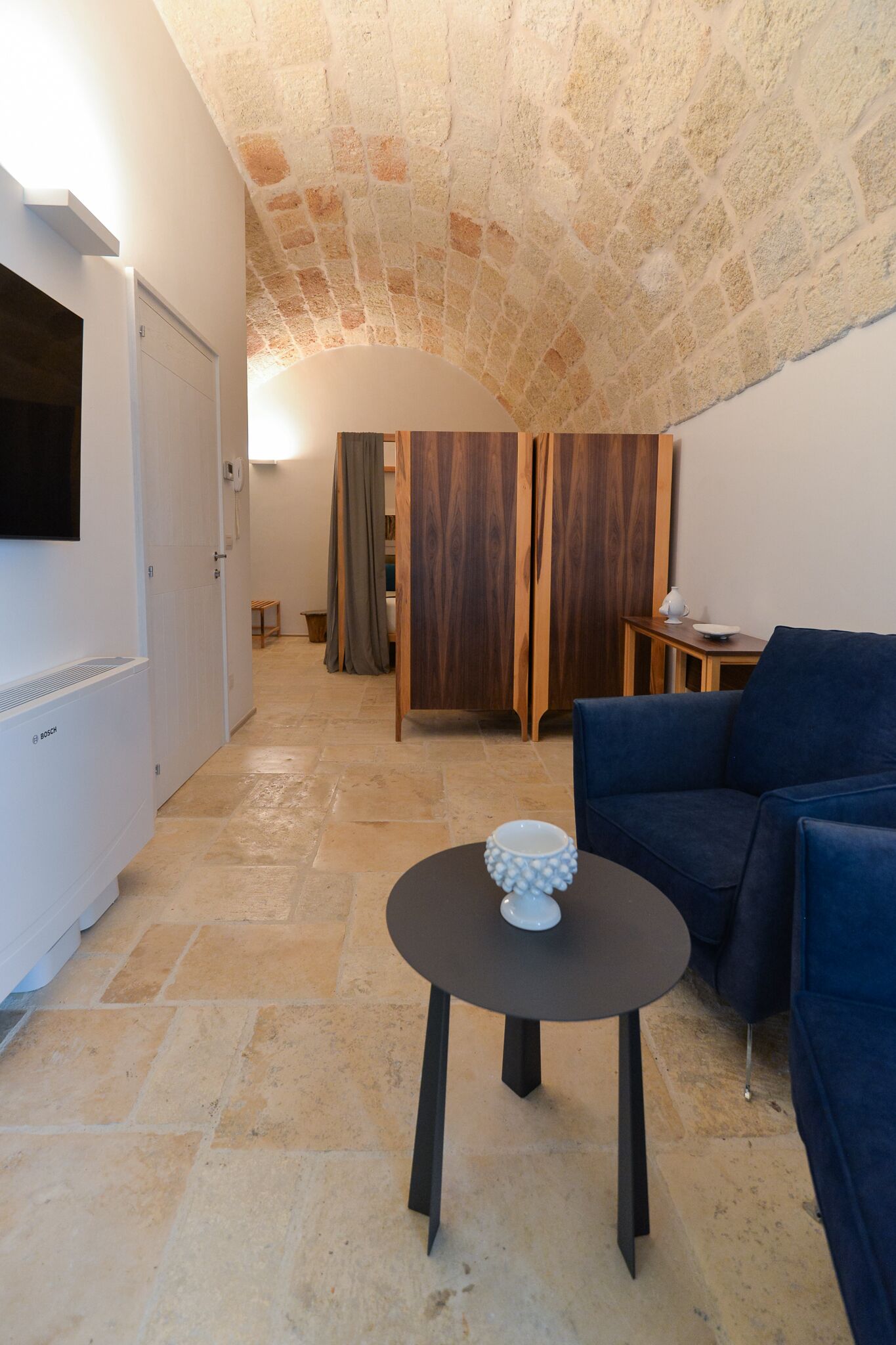 Una habitación acogedora con techo de piedra, un sofá azul, una mesita redonda con un cuenco blanco y armarios de madera.