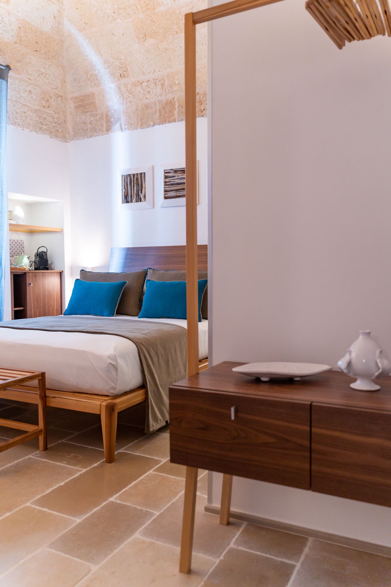A modern hotel room with a large bed, wooden headboard, and a desk with a lamp.