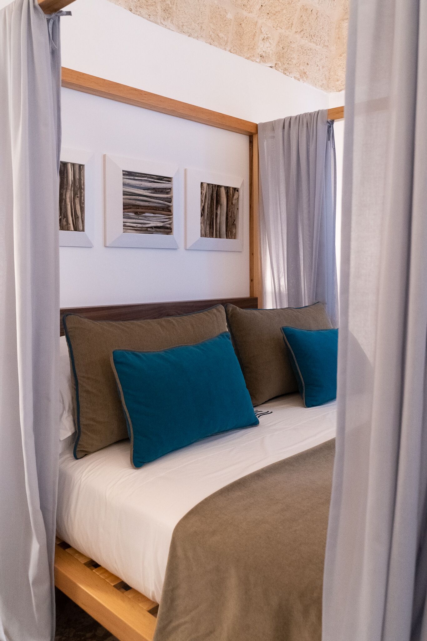 A bedroom with a wooden headboard, a bed with white bedding and two blue pillows, and three framed pictures on the wall.