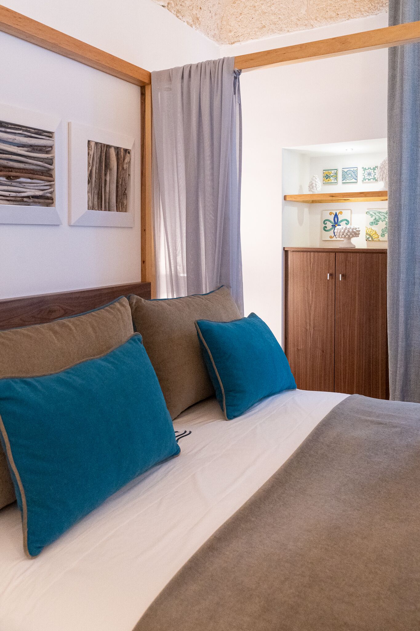 Un dormitorio con cama, dos almohadas, cabecera de madera, armario y estante con objetos decorativos.