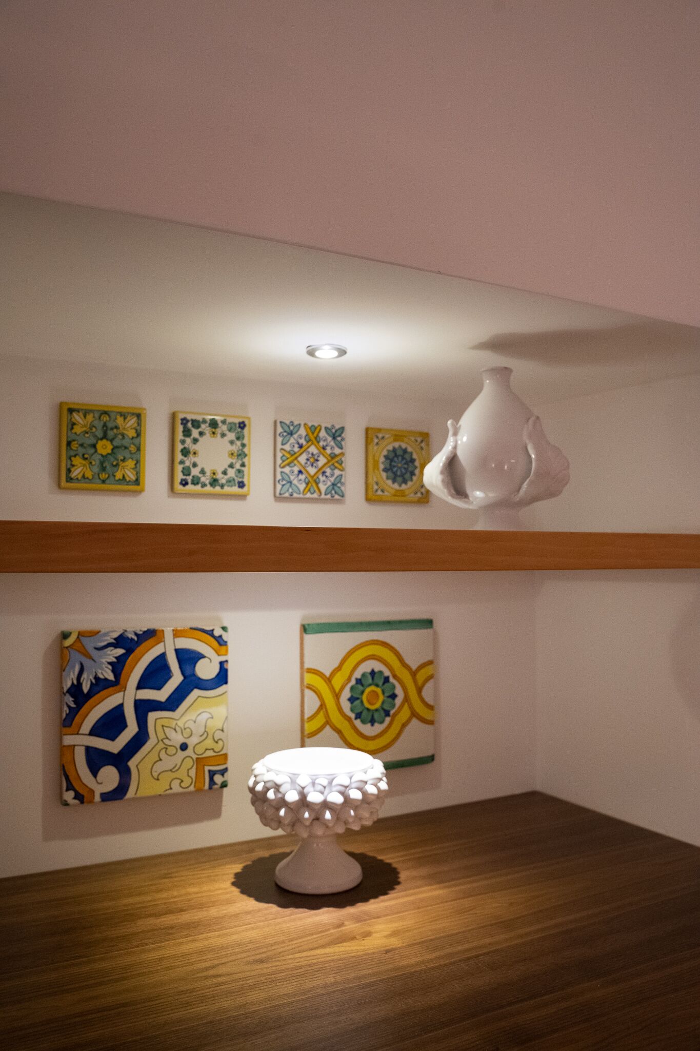 Een kamer met een houten vloer, een witte tafellamp en vier ingelijste kunstwerken aan de muur.