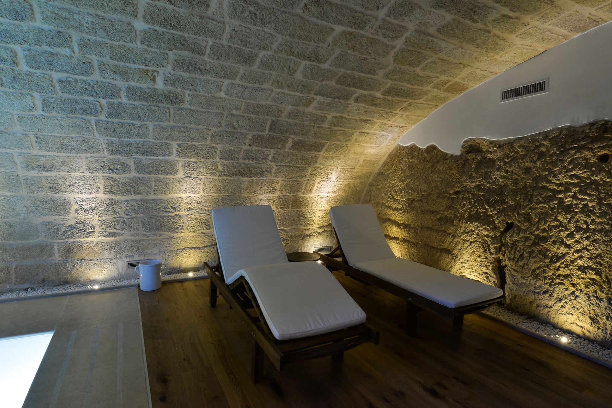 A stone-walled sauna with two wooden loungers and a small bucket.