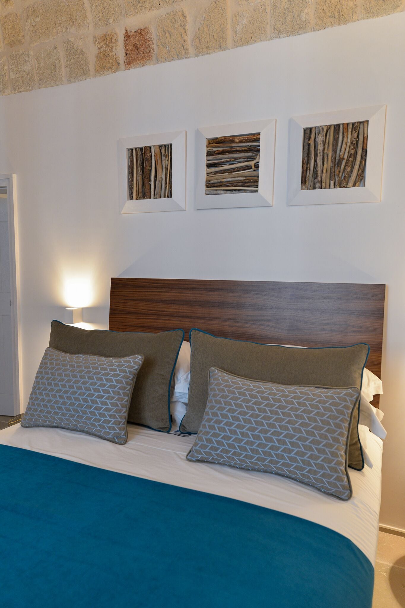 A neatly made bed with patterned pillows, a wooden headboard, and three framed artworks on the wall above.