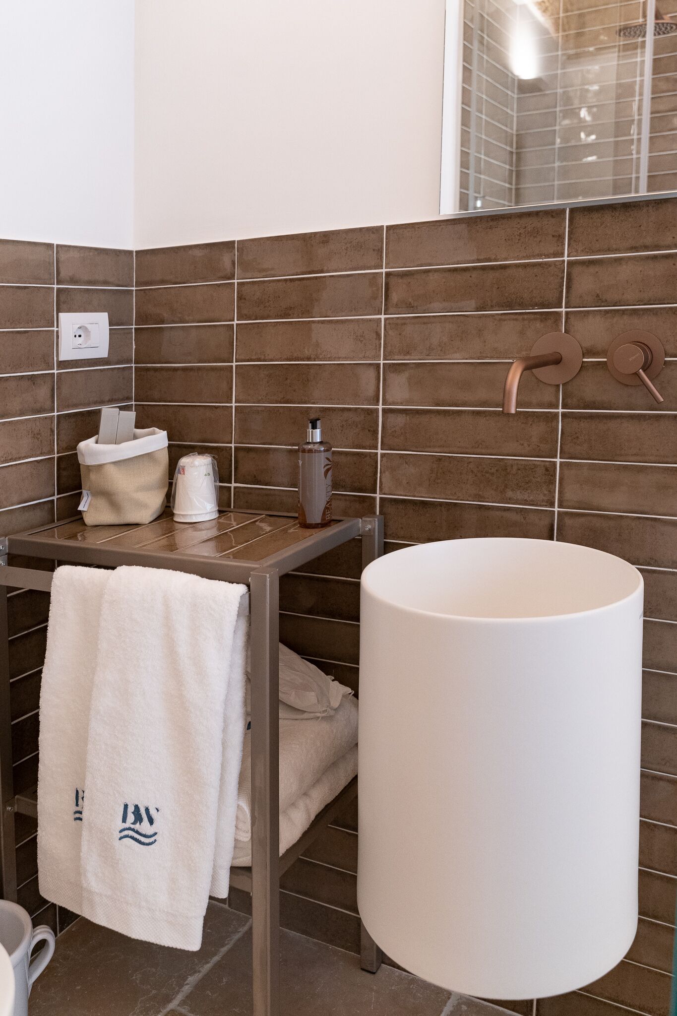 Un baño con un lavamanos grande y blanco, un perchero con una toalla blanca y una botella de champú sobre una estantería.
