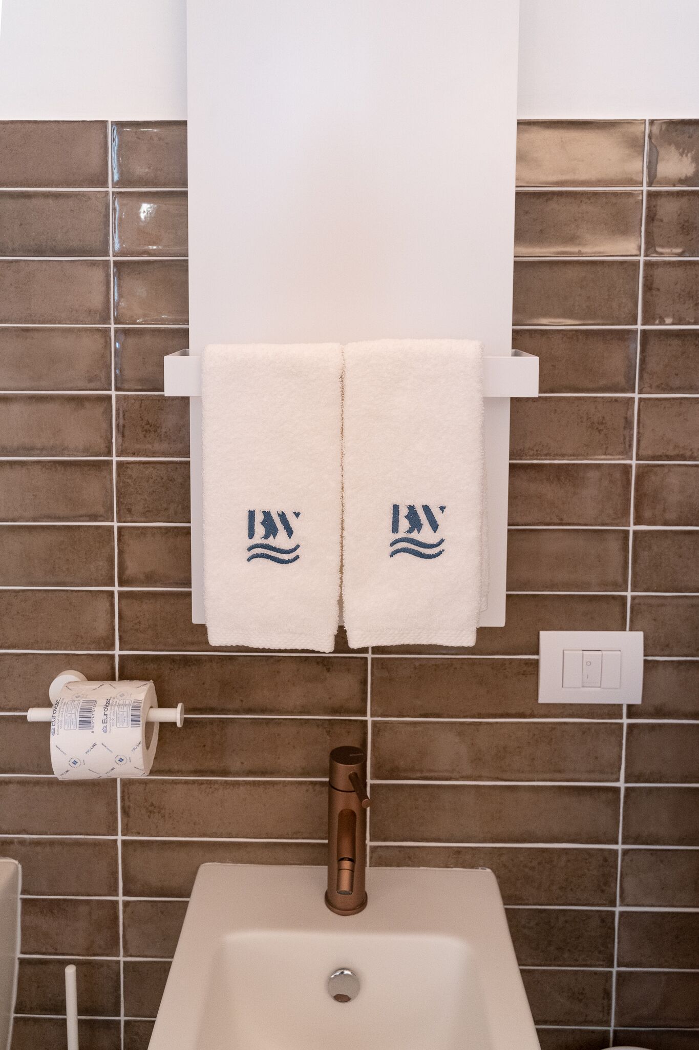 A bathroom with a white sink, two towels hanging on a rack, and a toilet paper holder.