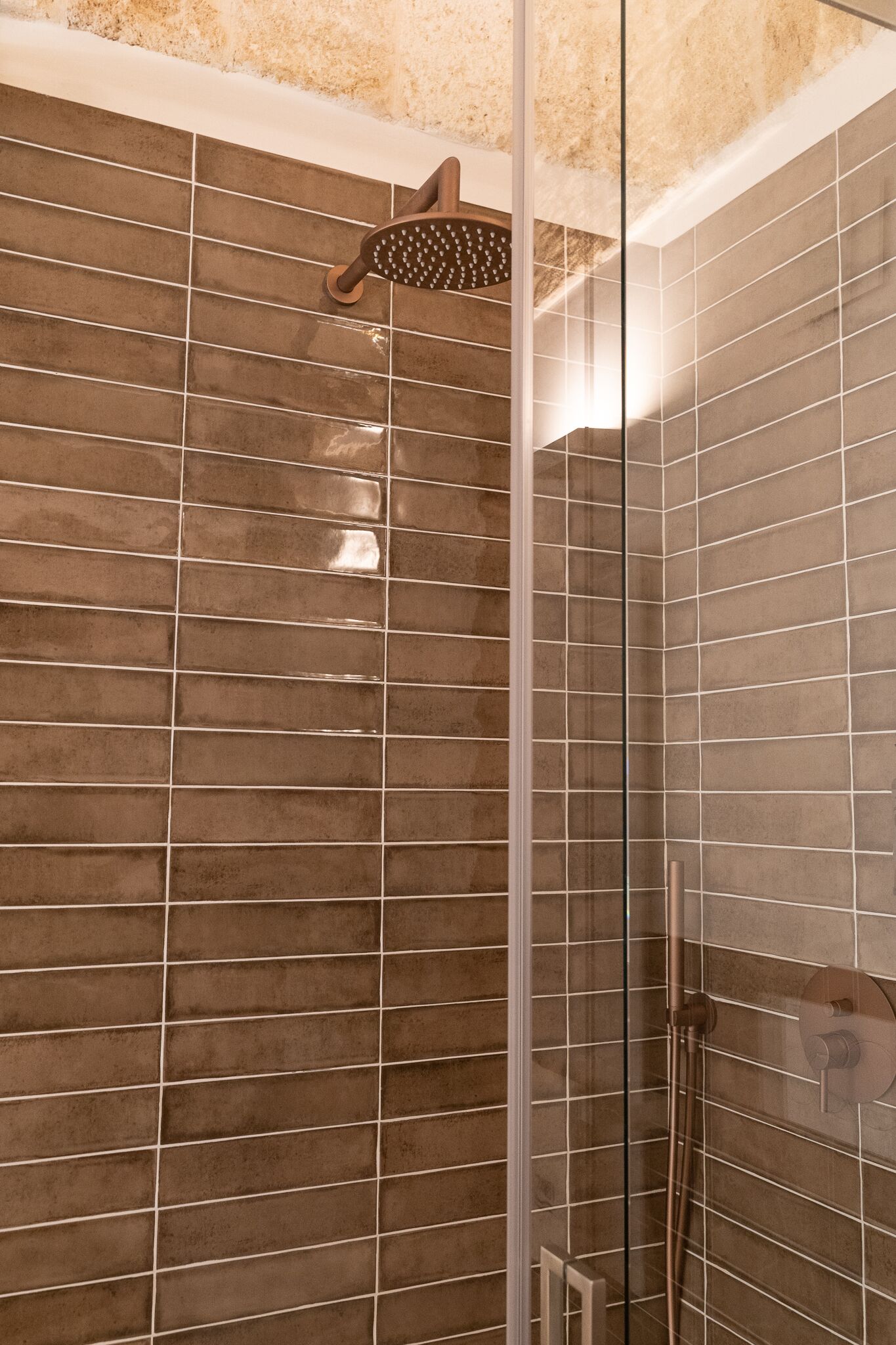 Un área de ducha con mampara de vidrio, paredes con azulejos y un cabezal de ducha de mano.