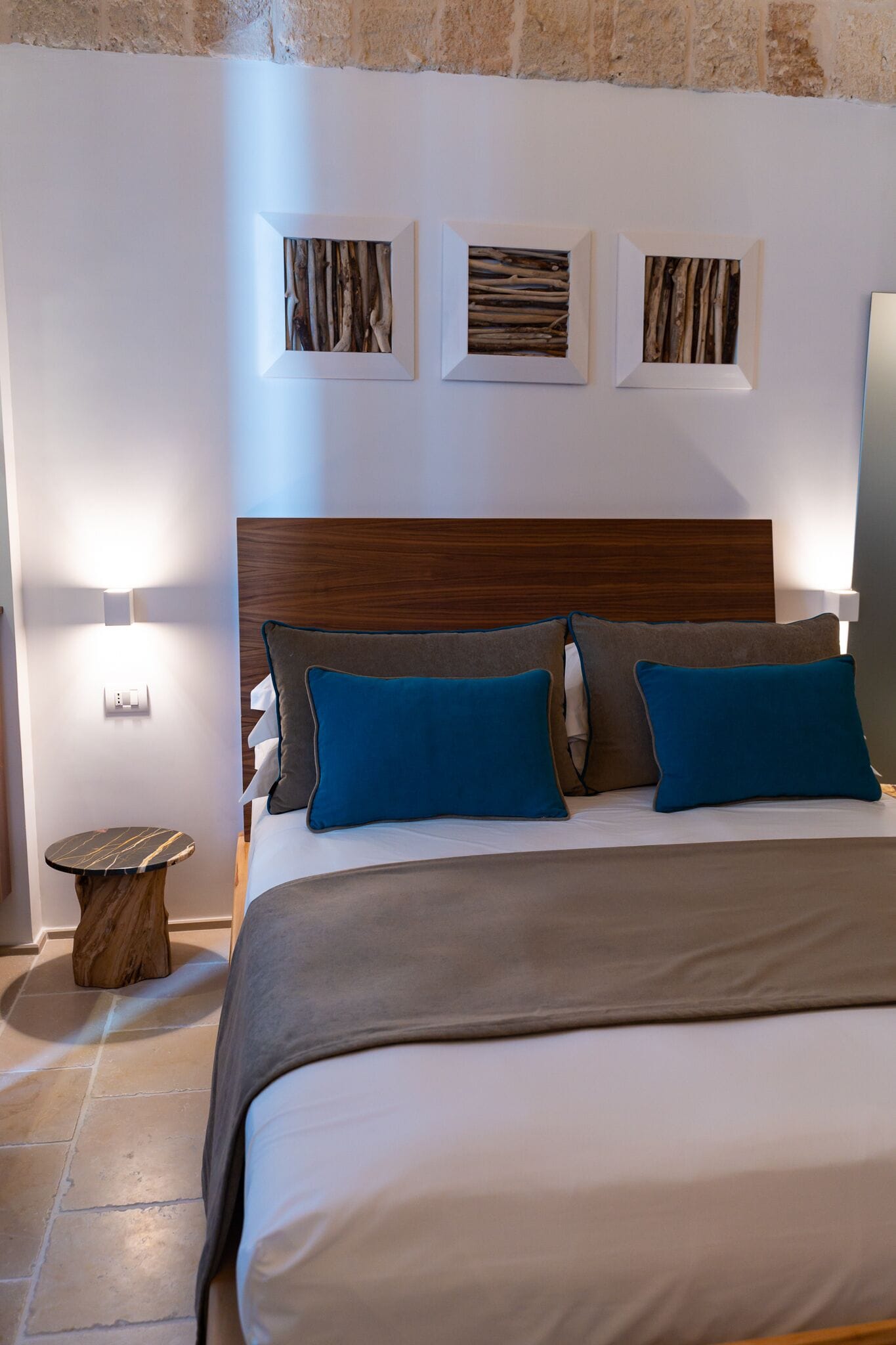 Un dormitorio ordenado con cabecera de madera, una mesita redonda y tres cuadros enmarcados en la pared.