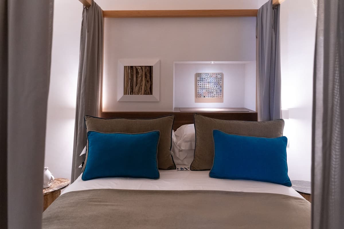 Un lit bien fait, avec deux oreillers bleus, une tête de lit en bois et deux lampes fixées au mur.