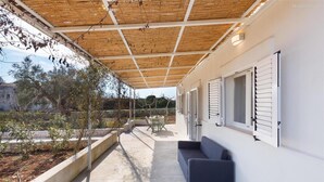 A covered outdoor area with a concrete floor, a dark-colored sofa, and a table with chairs. - 805 La Murreddina by Barbarhouse (Ostuni)