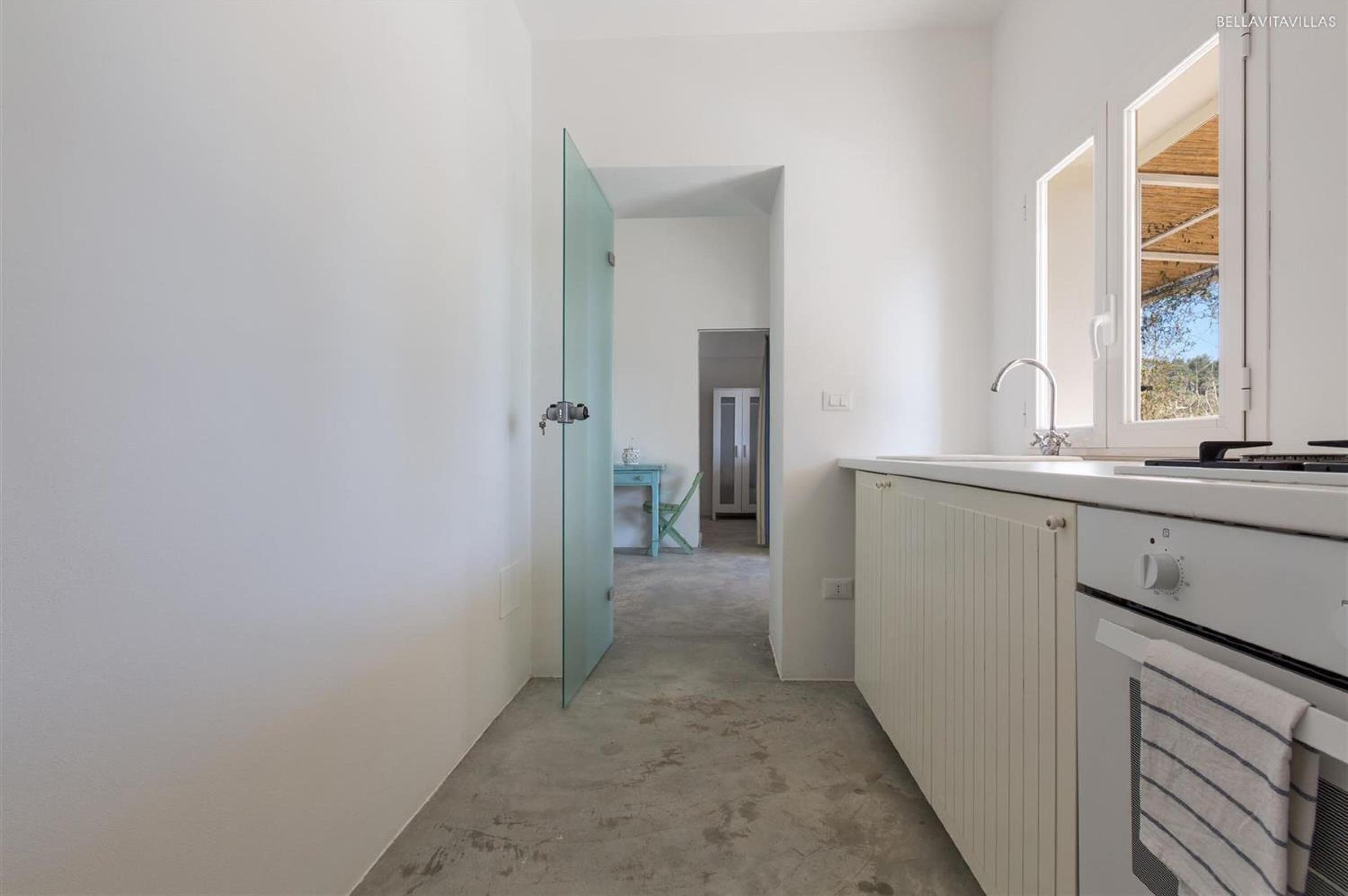 A narrow hallway leading to a kitchen with white cabinets and a window.