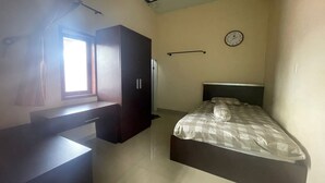A bedroom with a bed, a desk, a wardrobe, a window, and a wall clock. - Hotel O Syukur 07 Syariah (Medan)