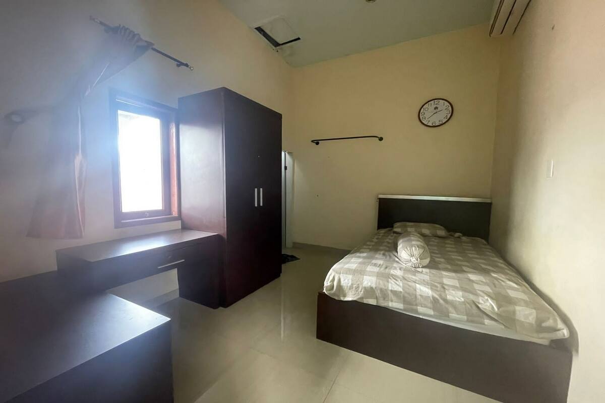 Ein Schlafzimmer mit Bett, Schreibtisch, Kleiderschrank, Fenster und Wanduhr.