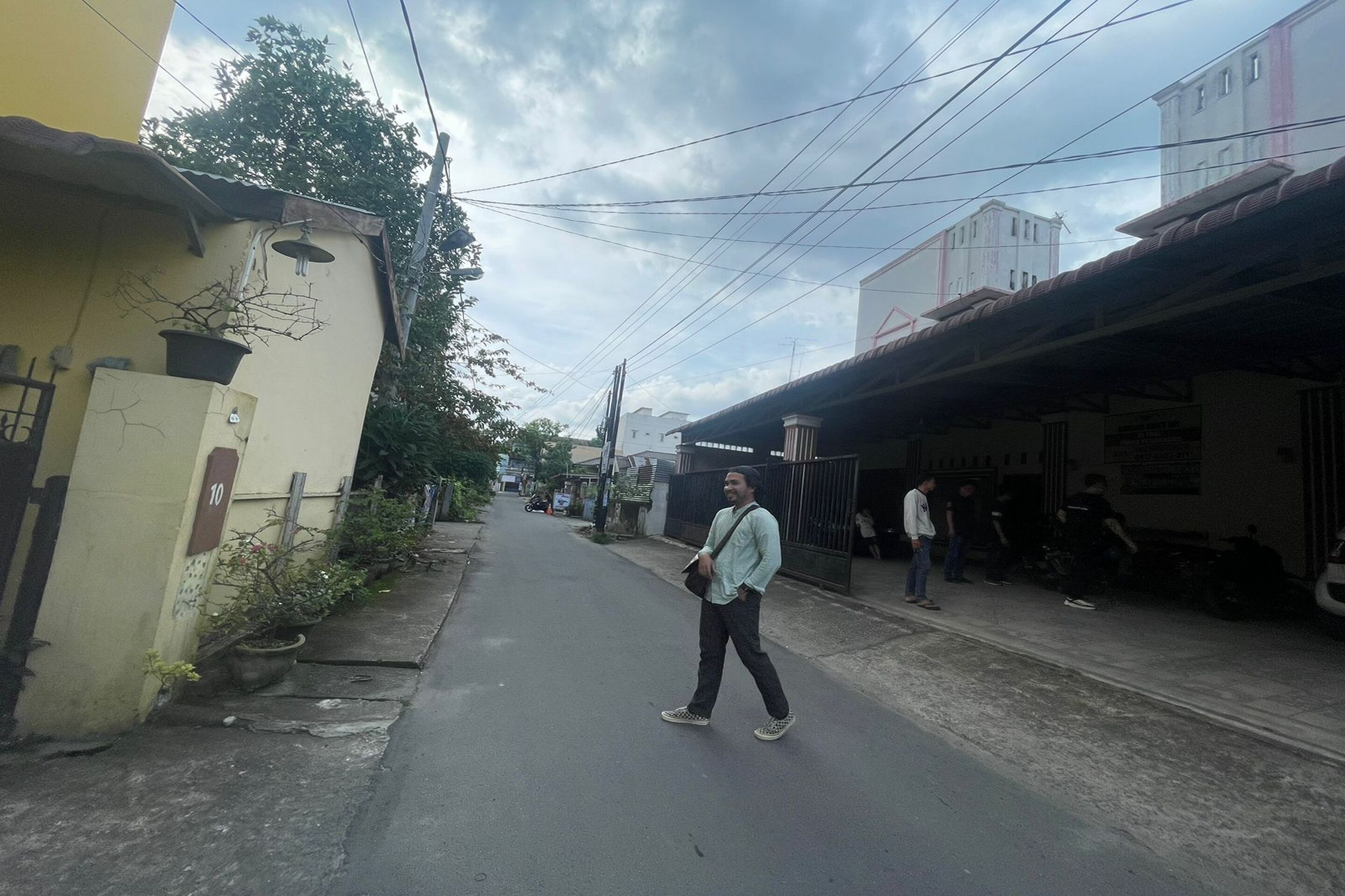 A narrow street with buildings on both sides, a man walking, and some parked vehicles.
