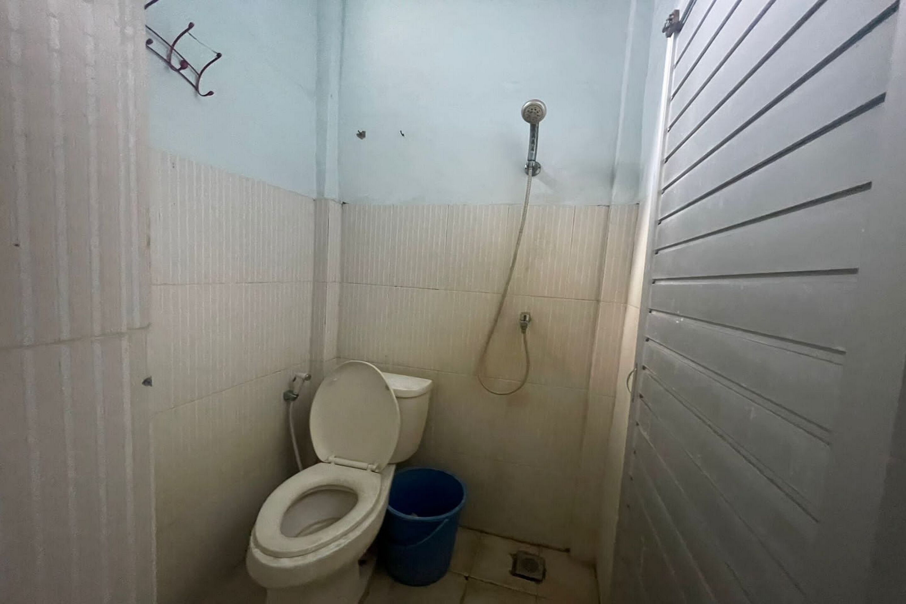 Ein kleines, schmales Badezimmer mit Toilette, Dusche und einem blauen Eimer.