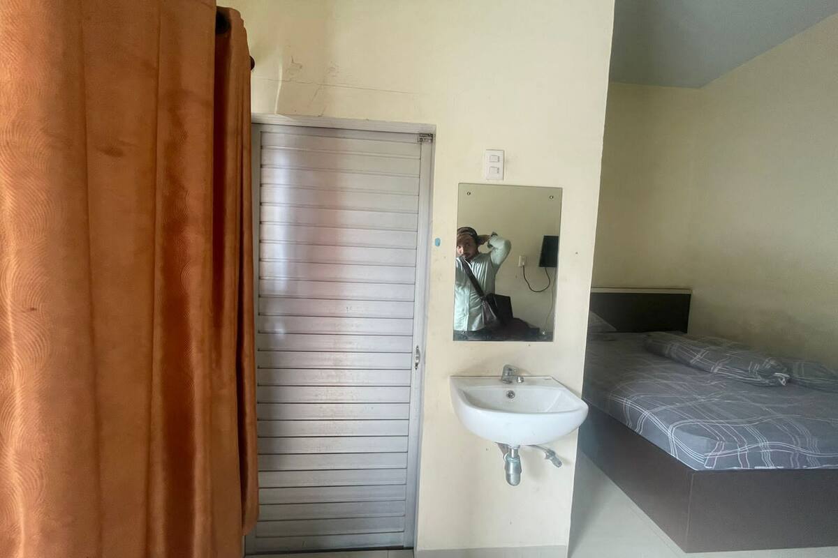 Ein Zimmer mit geschlossener Tür, einem Bett mit gemustertem Überwurf, einem weißen Waschbecken und einem Spiegel an der Wand.
