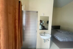 A room with a closed door, a bed with a patterned bedspread, a white sink, and a mirror on the wall.