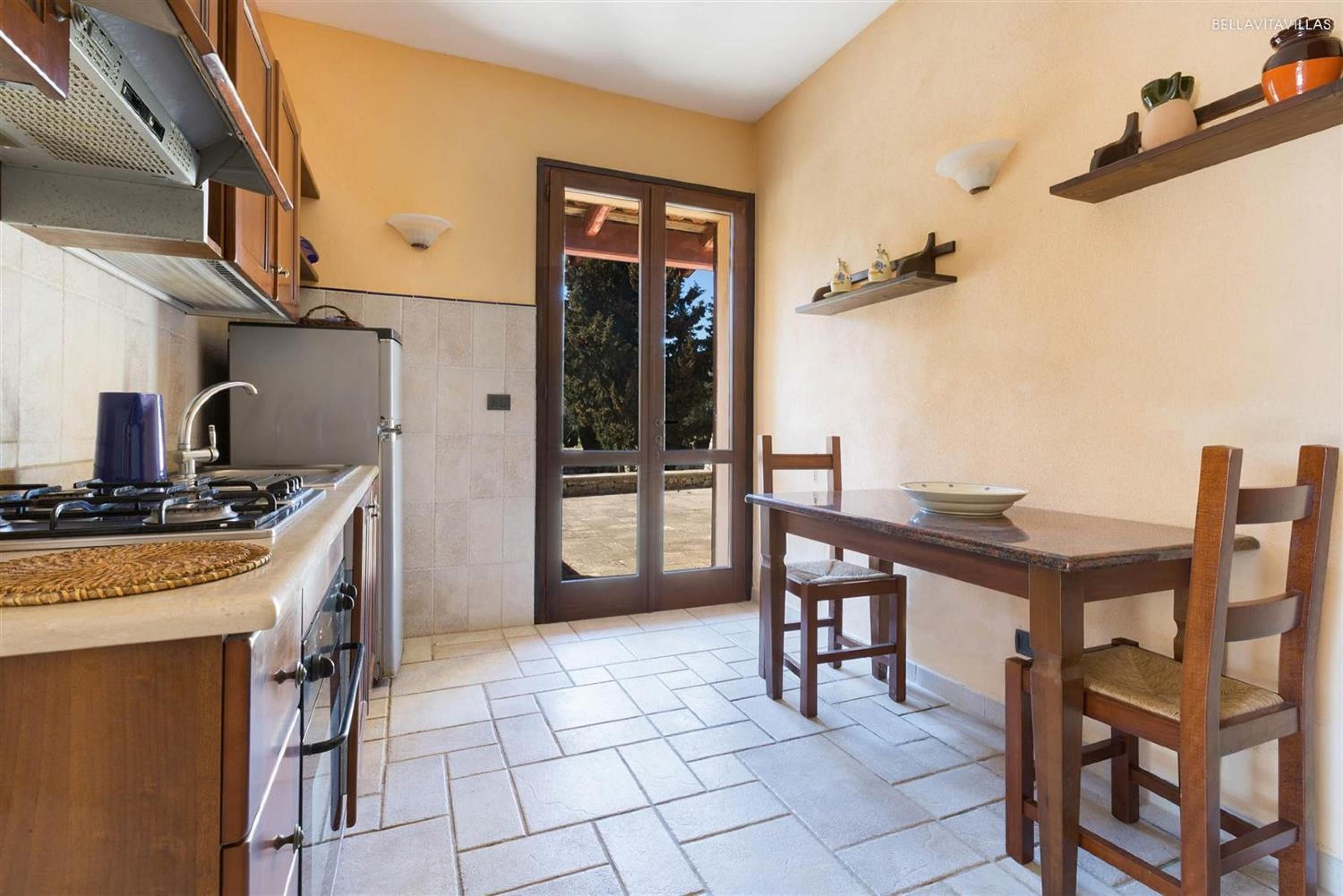 A kitchen with a gas stove, a refrigerator, a sink, and a dining area with a table and chairs.