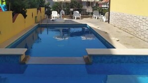 Ein Poolbereich mit Liegestühlen und Sonnenschirmen, umgeben von gelben Wänden und blauem Himmel.