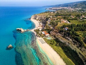 Luftaufnahme einer Küstenlandschaft mit Strand, Klippen und einem Wohngebiet.