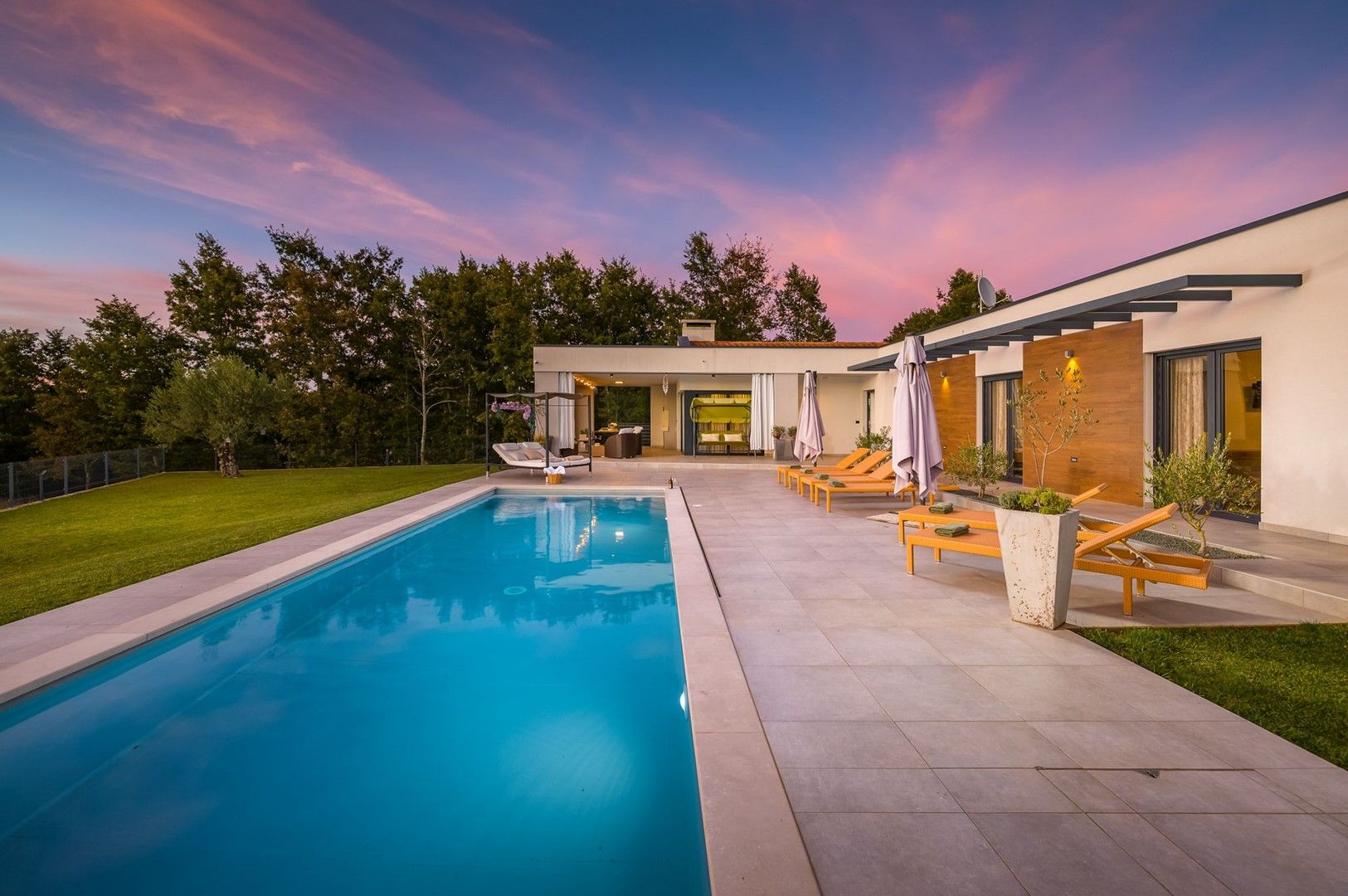 Un espace moderne aménagé au bord de la piscine, avec une piscine à eau claire, des chaises longues et un bâtiment contemporain doté de grandes fenêtres.