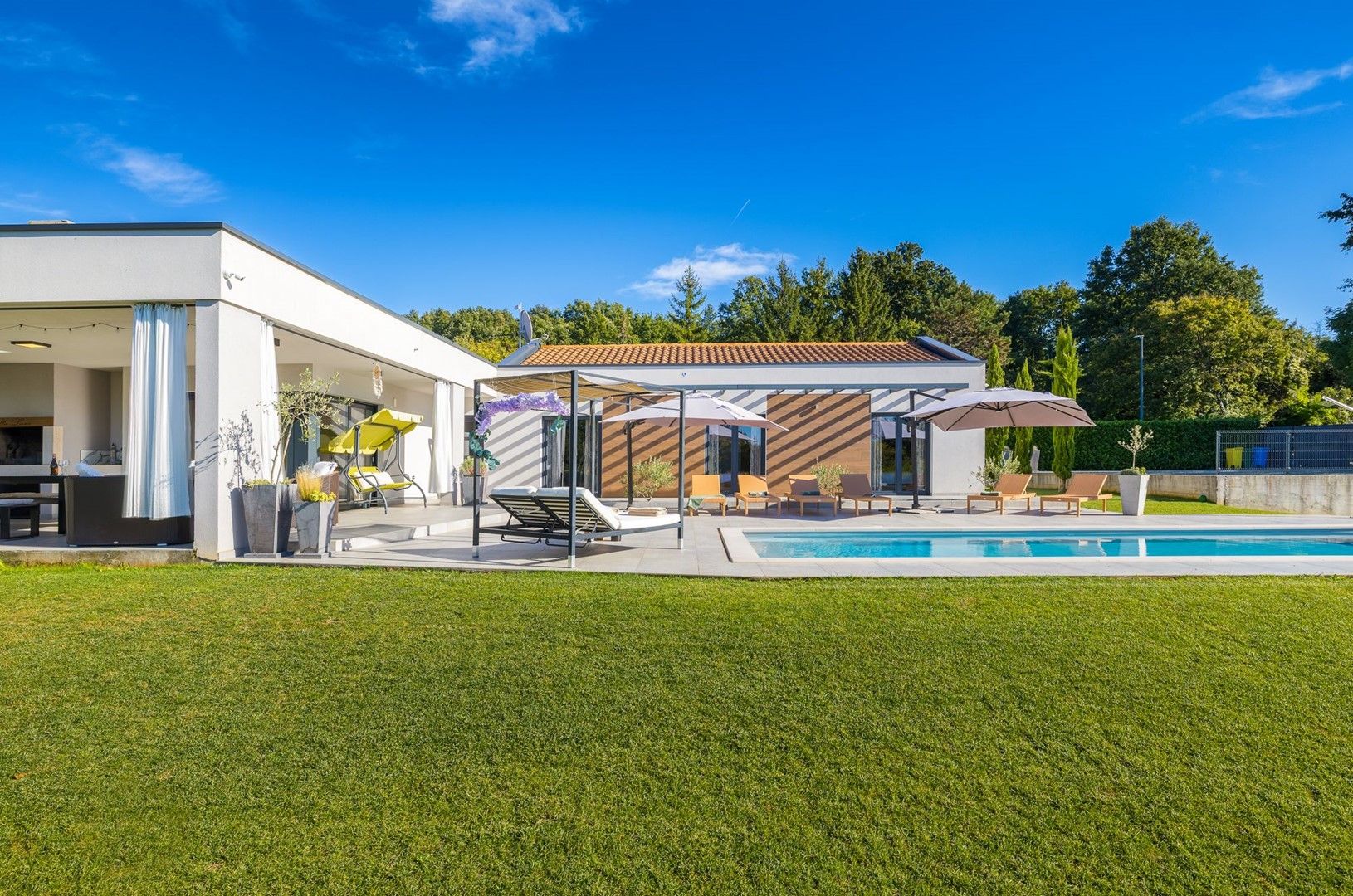 A modern house with a swimming pool, outdoor seating, and a well-maintained lawn.