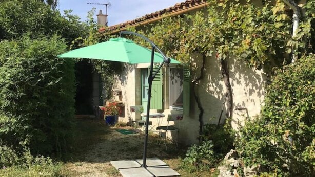 A patio area with a green umbrella, a stone wall, and a small table. - Pavillon de Chasse, Gîte 2/4 Pers (Blanzay)