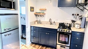 Cocina compacta equipada con refrigerador, microondas, fregadero, estufa y diversos utensilios.