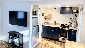 Una cocina compacta con televisor, microondas, refrigerador, estufa y piso de madera.