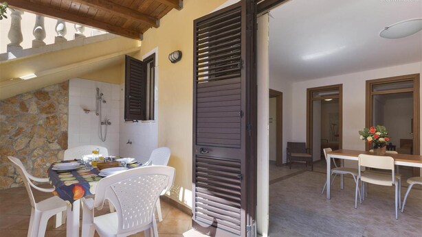 Un espacio habitable abierto con una mesa de comedor preparada para dos personas, una pared de piedra y un techo de madera.