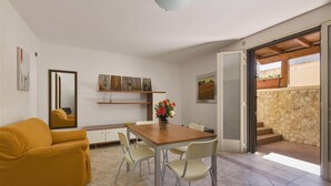 Una sala moderna con un sofá, una mesa de comedor con sillas, un espejo, obras de arte en las paredes y vistas al exterior.