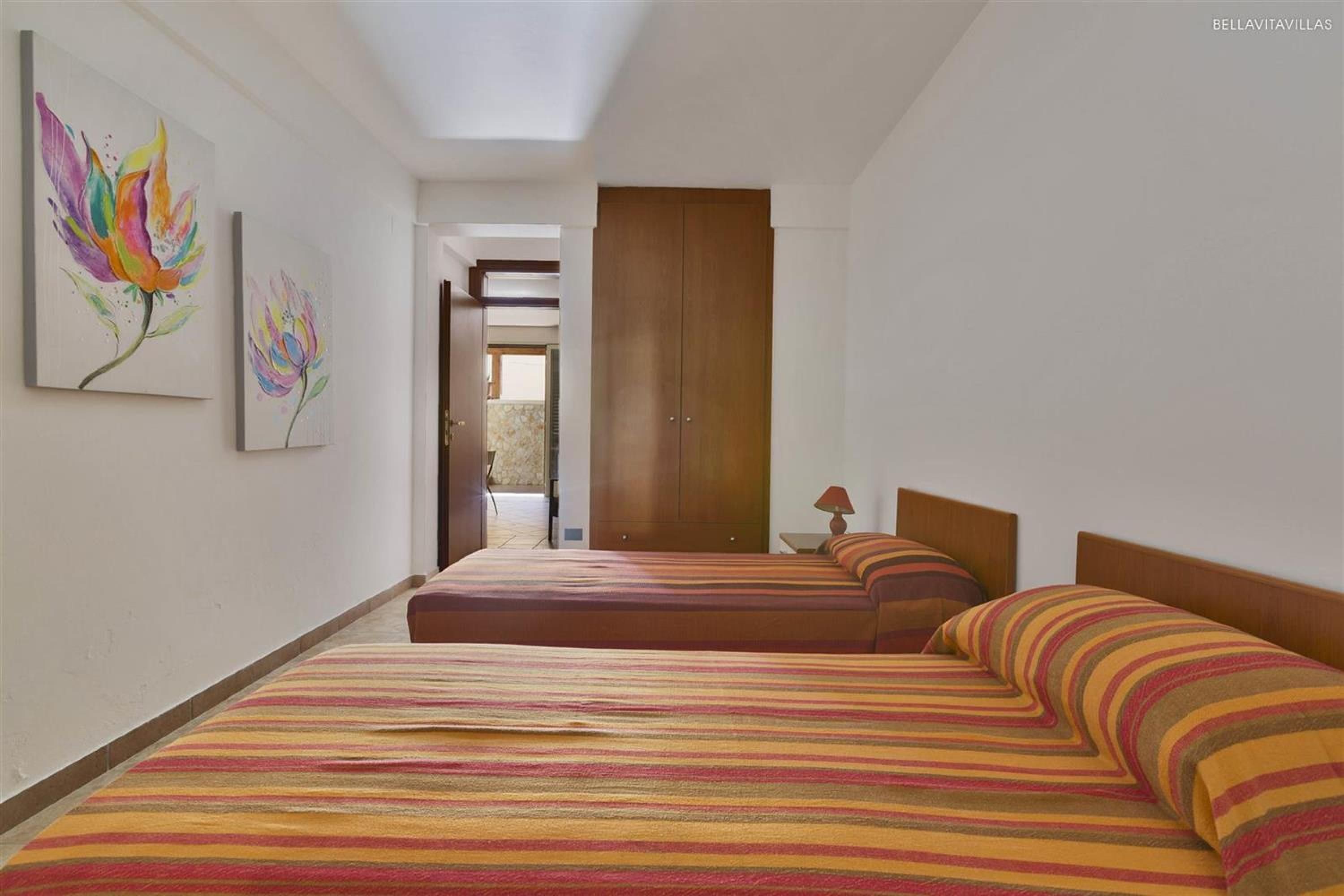 A bedroom with two beds, a wooden wardrobe, and two paintings on the wall.