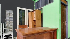 A room with a wooden desk, a white chair, and a window with patterned glass. - Hotel O Juan Kostel 3 (Purwokerto)