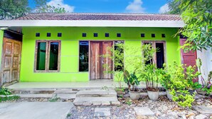 A green house with a tiled roof, wooden doors, and windows. There are potted plants in front. - Hotel O Juan Kostel 3 (Purwokerto)